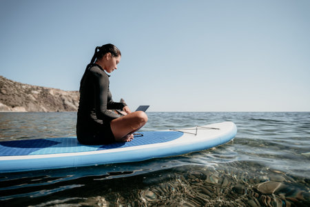 Woman Paddleboard Laptop Sea Relaxing, Woman relaxes on a paddleboard in the sea while using her laptop.の写真素材
