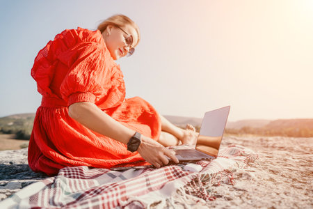 Woman in Red Dress Working on Laptop in Natureの写真素材