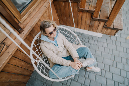 Woman in a Beige Coat Relaxing in a Hanging Chairの写真素材