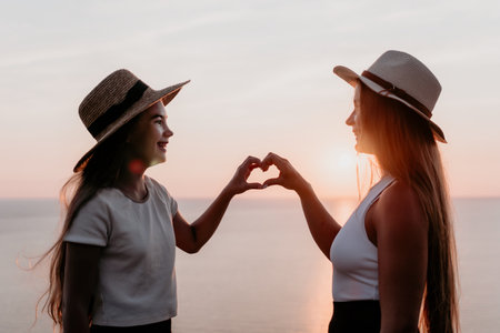 Two Women in Straw Hats Making a Heart Shape at Sunsetの写真素材