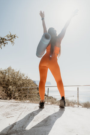 Woman in Orange Workout Outfit Raises Arms with Yoga Matの写真素材