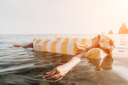 Woman Float Inflatable Ocean - Woman relaxing on a yellow and white striped inflatable float in the...