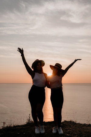 Two Silhouettes of Women in Hats Against a Sunsetの写真素材