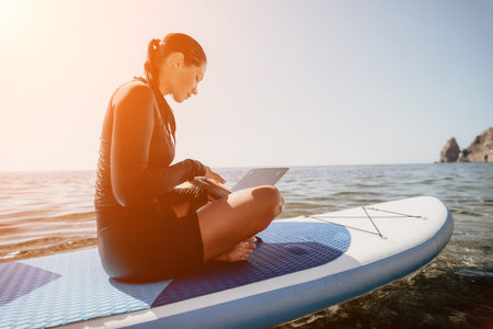 Woman Laptop Paddleboard Working remotely on a stand up paddleboard in the ocean at sunset.の写真素材