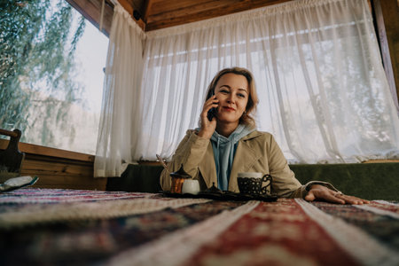 Woman Talking on Phone and Enjoying Coffee in a Cozy Cafeの写真素材
