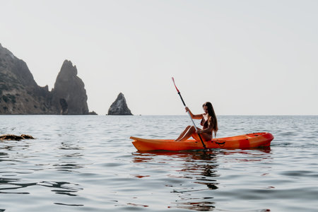 Kayaking Woman Sea Coastline - A woman paddles a kayak in the sea with a rocky coastline in the background.の写真素材