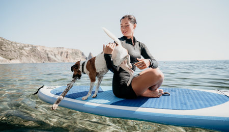 Woman Dog Paddleboard Beach Summer: Woman and dog paddleboarding on blue water with clear sky.の写真素材