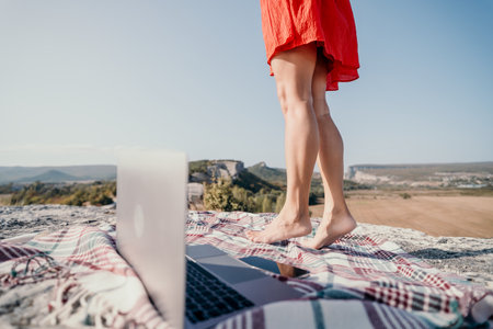 Woman in Red Dress Standing on a Clifftop with Laptopの写真素材