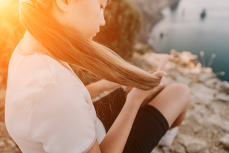 Young Girl With Long Brown Hair Sitting On A Cliff Overlooking The Oceanの写真素材