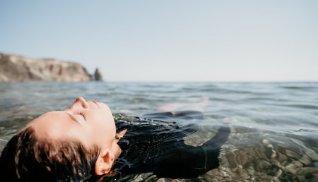 Woman Floating Water Ocean - Woman relaxes in the ocean water near a rocky cliff on a sunny day.の写真素材