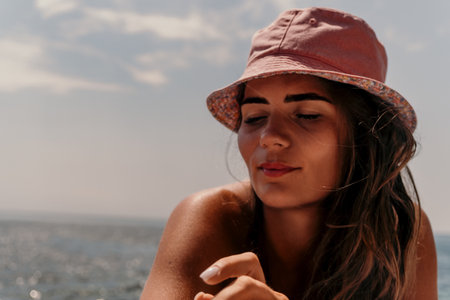 Woman, Pink Hat, Ocean: Close-up of a young woman wearing a pink hat, gazing thoughtfully towards the sea on a sunny day.の写真素材