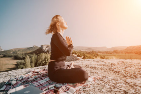 Woman in Black Meditates on a Mountaintop with Laptop and Blanketの写真素材