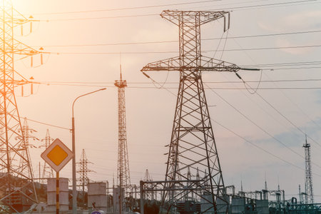 High voltage electric distribution network at sunset. Power transmission lines on supports with ceramic insulators and transformers at large electrical distribution substationの写真素材