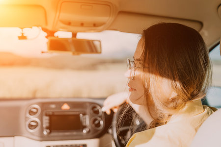 A woman in a yellow shirt is driving a car. She is wearing glasses and has her hands on the steering wheelの写真素材