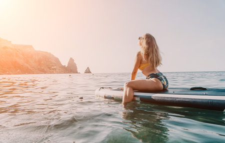Woman Paddleboard Ocean View - A young woman sits on a paddleboard looking out at the ocean and rocky cliffs.の写真素材