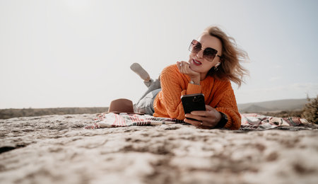Woman in Orange Sweater Relaxing on a Rock with a Phoneの写真素材