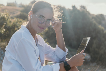 Woman Glasses Laptop - Smiling woman wearing glasses and using a laptop outdoors on a sunny day.