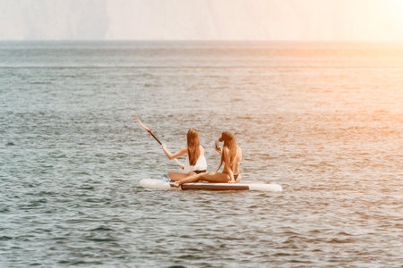Women Paddleboard Ocean Sunset - Two women relax on a paddleboard in the ocean at sunset.の写真素材