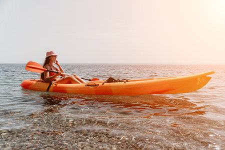 Kayaking Woman Sea Sunset - A woman in a pink hat kayaks on a calm sea under a sunset sky.の写真素材