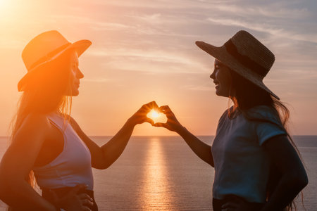 Two Women Silhouetted Against a Sunset, Making a Heart Shape With Their Handsの写真素材