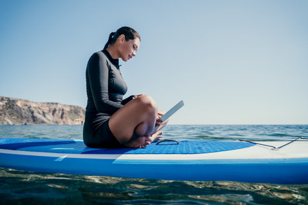 Woman, Laptop, Paddleboard - Working on a laptop while sitting on a paddleboard in the ocean.の写真素材