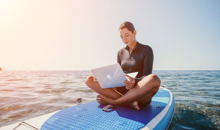Woman Laptop Paddleboard Ocean - Woman working on laptop while paddleboarding on the ocean.の写真素材