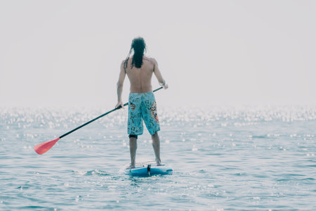 Man Paddleboarding Ocean Water Sport - A man paddleboards on the ocean during a calm, overcast day.