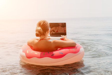 Woman Beach Laptop Working Remotely on Vacation in Donut Floatの写真素材