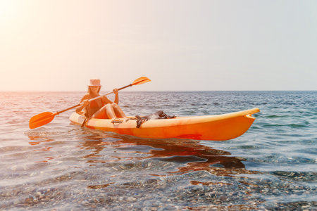 Kayaking Woman Sea Sunset - A woman kayaks on the calm sea at sunset, enjoying a peaceful water activity.の写真素材