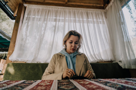 Woman in a Beige Coat Looks at a Small Black Objectの写真素材