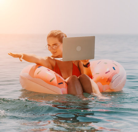 Woman Laptop Beach - Working on a laptop while floating on an inflatable ring in the ocean at sunset.の写真素材