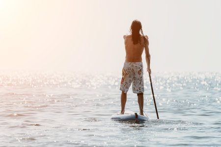 Man Paddleboarding Ocean Sunset - A man enjoys paddleboarding in the ocean at sunset.