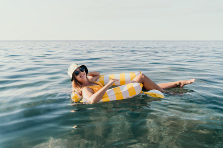 Woman Floating Inflatable Ocean Summer: A woman relaxes on a yellow and white inflatable float in the ocean on a sunny day.の写真素材