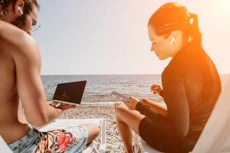 Couple Beach Laptop - Young couple working on laptop while sitting on beach chairs at sunset.の写真素材