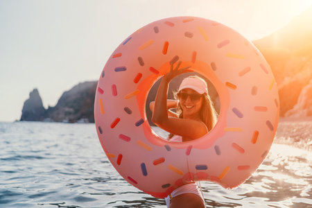 Woman, donut float, ocean. Smiling woman on summer vacation stands in the sea with a large donut-shaped inflatable, bright sun, copy space.の写真素材