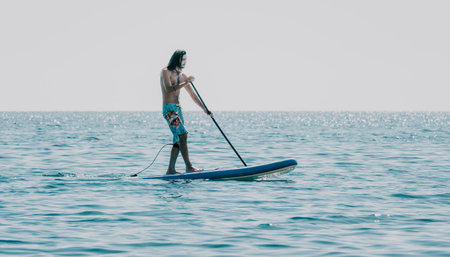 Man Sup Sea. Strong athletic man learns to paddle sup standing on board in open sea ocean on sunny...