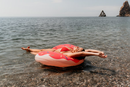 Woman, Donut Float, Beach: Relaxing on a pink donut float in the sea.の写真素材