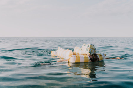 A person floats in the ocean with several wrapped items as a makeshift flotation device.