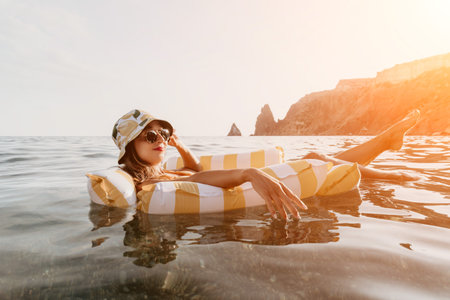Woman Beach Float Relaxation - A woman wearing a hat and sunglasses relaxes on a striped inflatable...