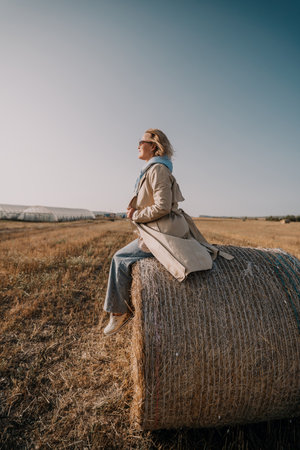 Woman Sitting on Hay Bale in Fieldの写真素材