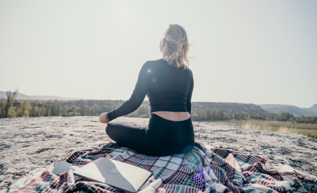 Woman Meditating on a Rocky Peak with a Laptopの写真素材