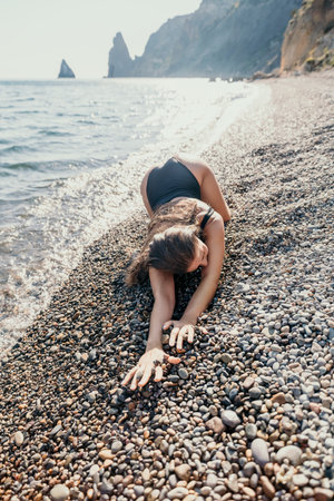 Woman in Black Swimsuit Reaching for Pebbles on a Beachの写真素材