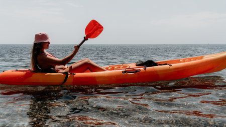 Kayaking Woman Ocean Paddle - Young woman paddling orange kayak in ocean on sunny day enjoying recreational activity.の写真素材