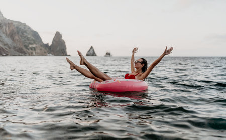 Woman floating sea. Joyful woman relaxes on pink donut in ocean near cliffs.の写真素材