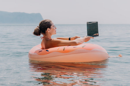 Woman, Laptop, Beach: Working remotely while floating in an inflatable ring in the ocean.