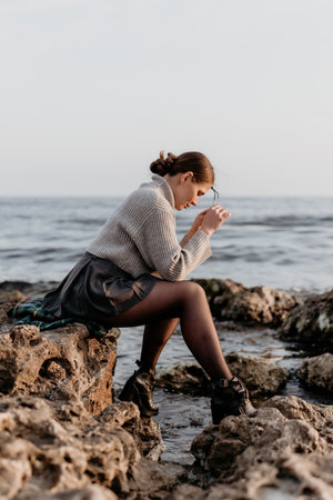 Woman sitting seashore. Pensive young woman resting on rocks by the ocean.の写真素材