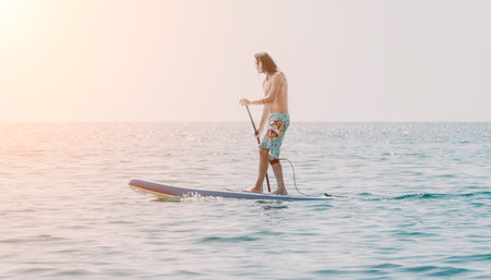 Man Paddleboarding Ocean Sunset - A man enjoys paddleboarding on a calm ocean during a beautiful sunset.の写真素材