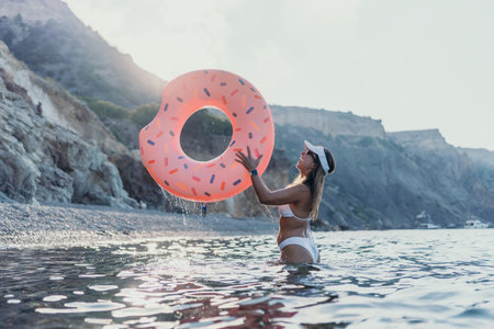 Woman donut float, happy woman enjoying summer vacation at rocky beach with copy space.の写真素材
