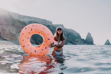 Woman, ocean, donut float, young woman stands in sea holding inflatable donut enjoying summer vacation at rocky coast.の写真素材