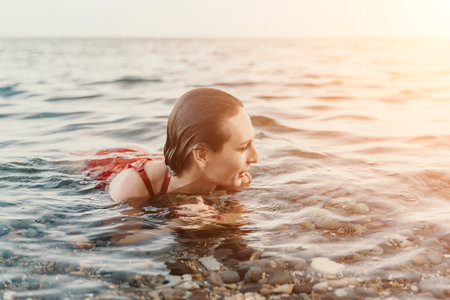 Woman swimming sea, enjoying tranquil vacation in clear water with pebbles at sunsetの写真素材